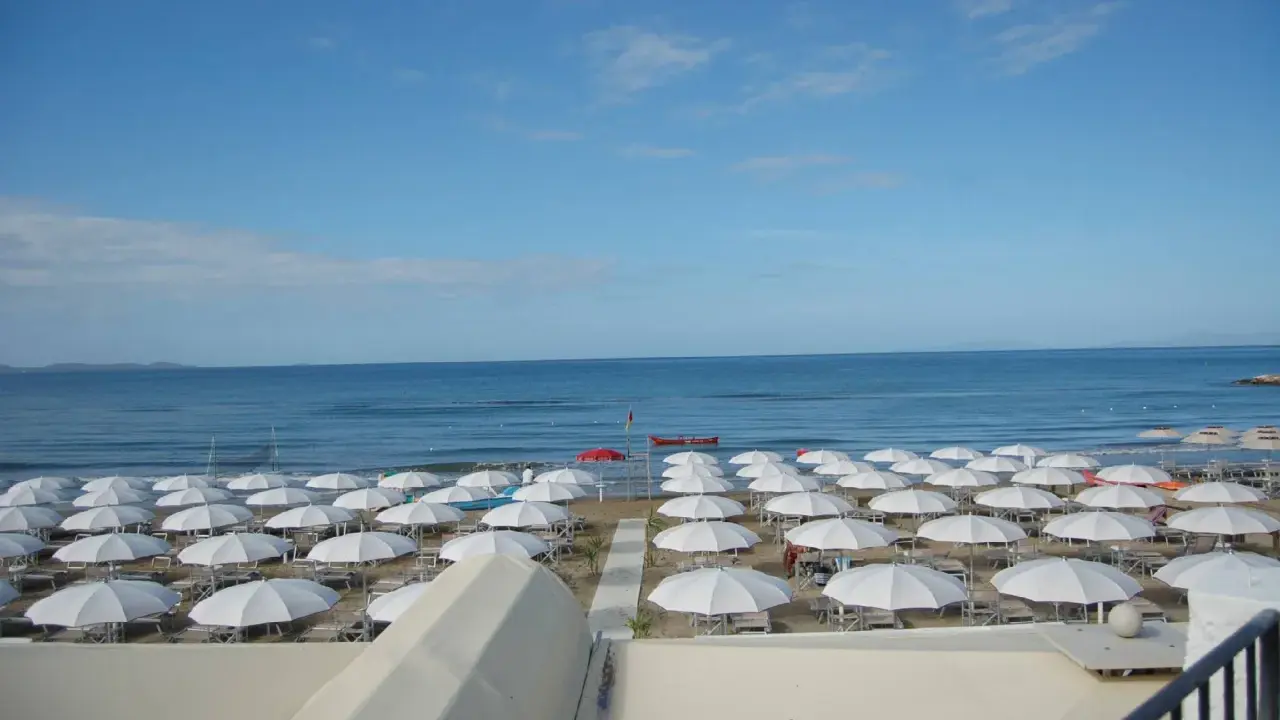 Spiaggia di **Marina di Follonica** con file ordinate di ombrelloni bianchi, mare azzurro e cielo sereno.