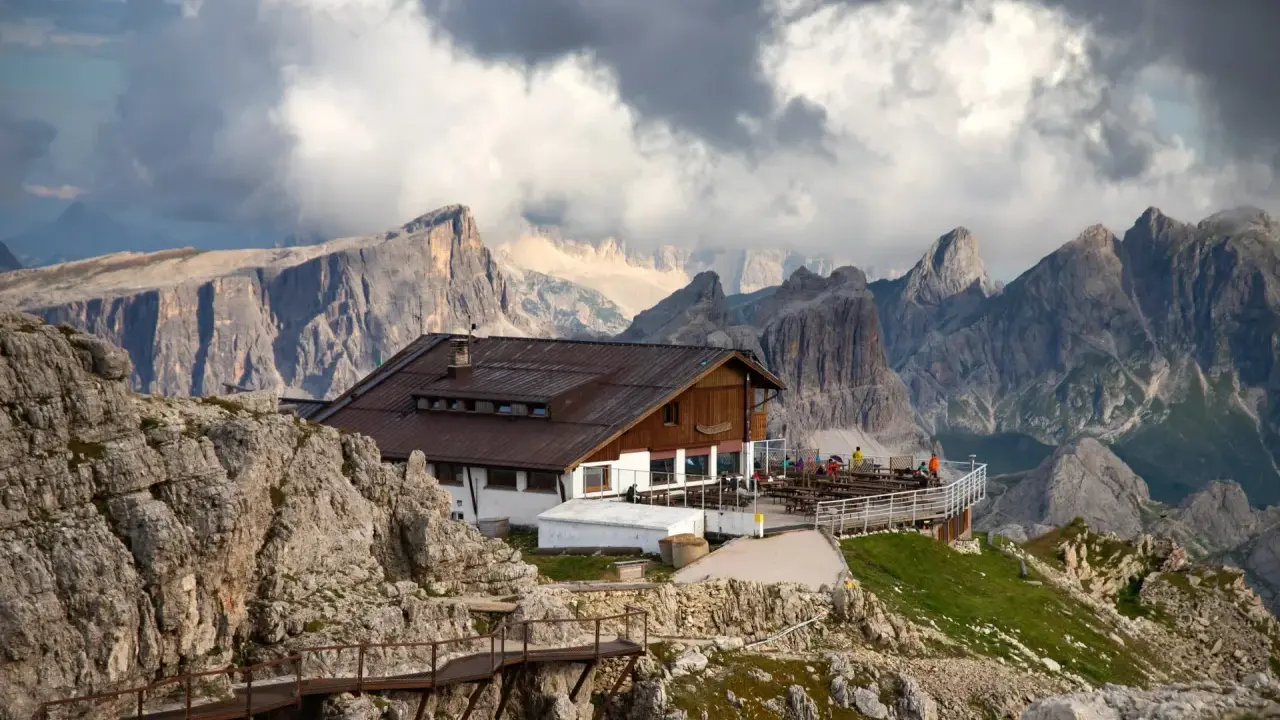 Rifugio alpino con terrazza panoramica, uno dei migliori rifugi dove dormire Dolomiti, incastonato tra imponenti vette rocciose e nuvole minacciose.