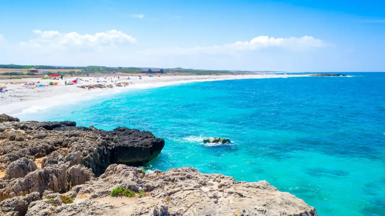 Scogli vulcanici e sabbia bianca su una spiaggia pop corn in Sardegna, con acque turchesi cristalline.