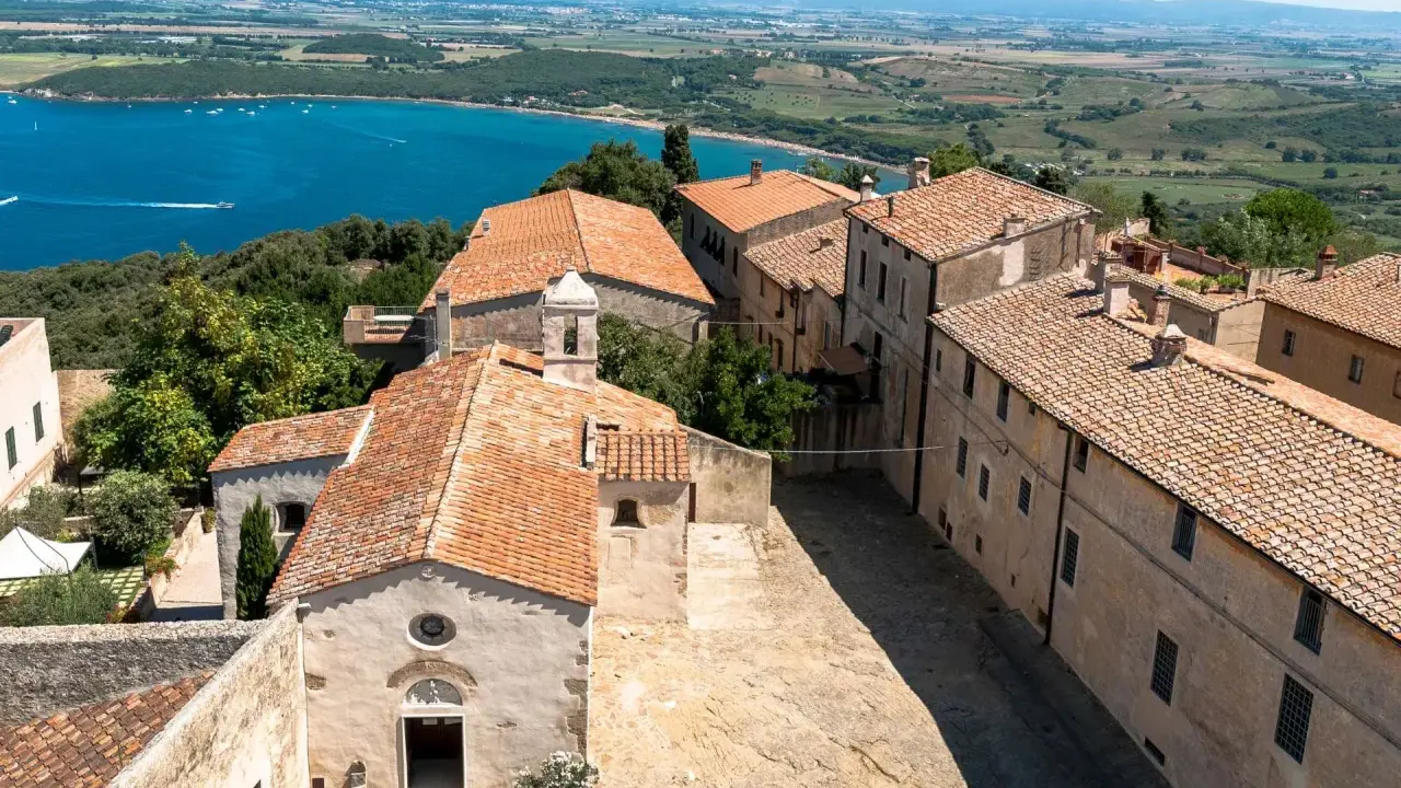 Vista dall'alto del populonia centro storico, con case dai tetti rossi e il mare blu sullo sfondo.