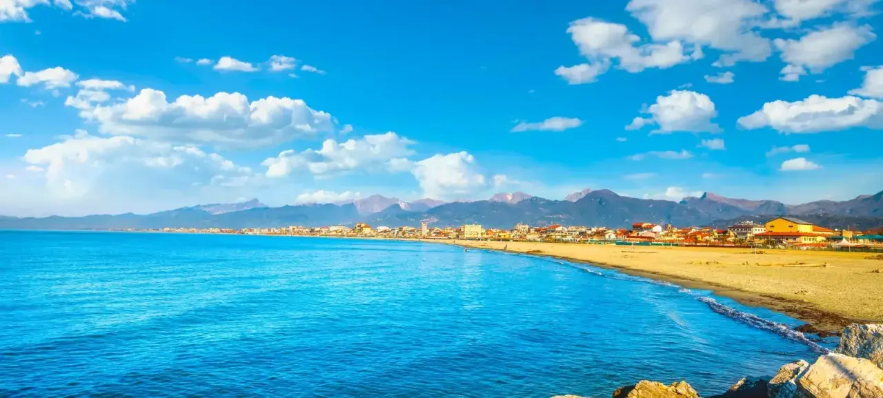 Spiaggia dorata e mare azzurro a Viareggio, con montagne sullo sfondo. Perfetto per scoprire cosa vedere a Viareggio in un giorno.