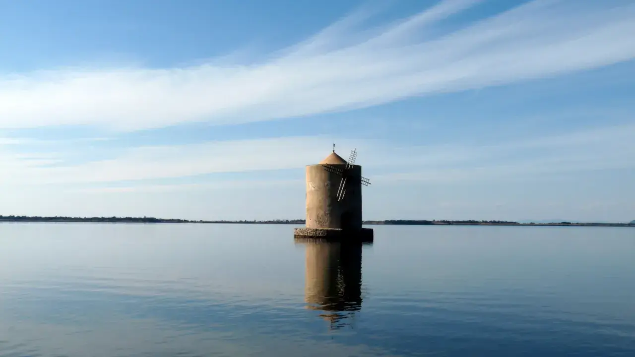 Mulino solitario nella laguna di Orbetello, con cielo azzurro e nuvole sottili.