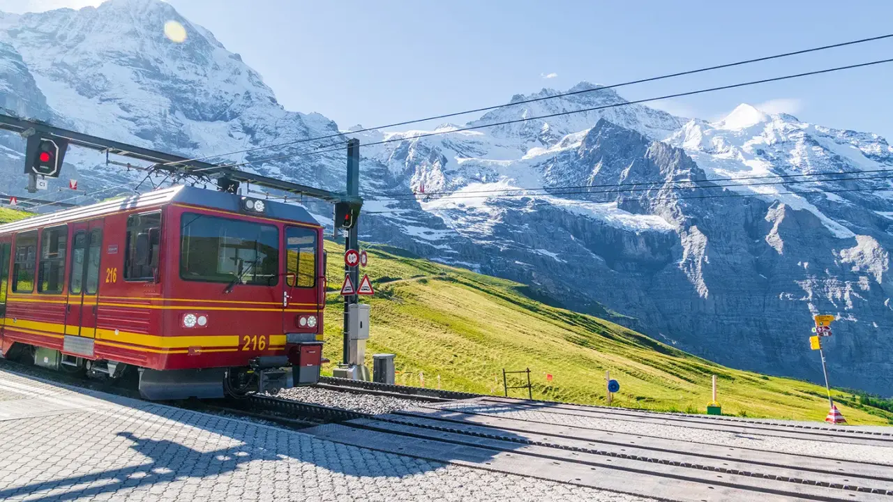 Treno rosso e giallo in stazione, con imponenti montagne innevate sullo sfondo. Un viaggio in treno tra le vette.