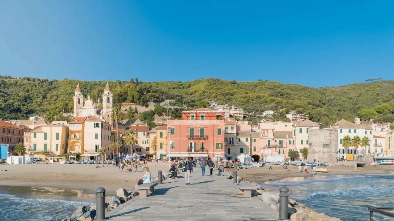 Laigueglia centro storico: case colorate affacciate sulla spiaggia, con una chiesa a due campanili e il mare azzurro.