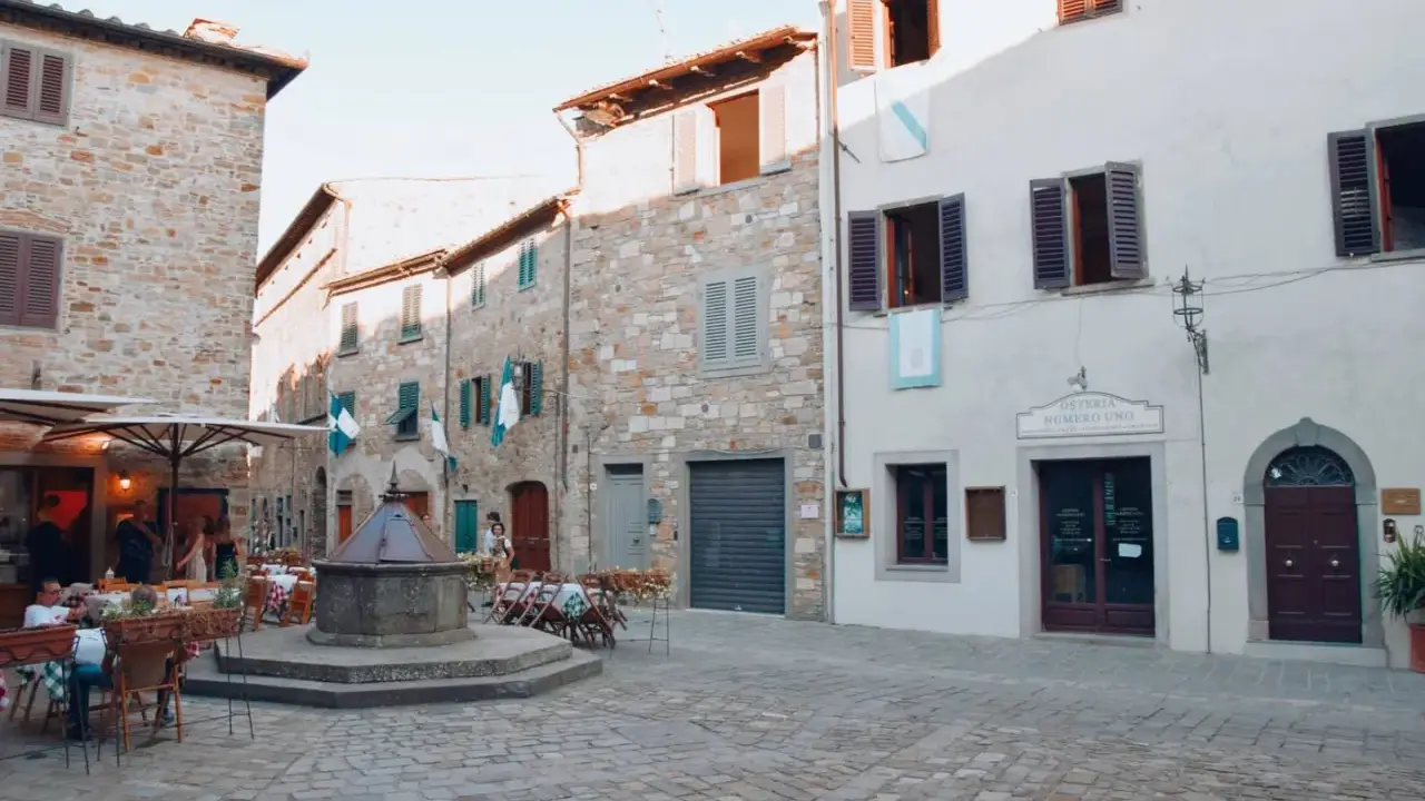 Piazza di San Donato in Poggio con pozzo antico, tavoli all'aperto e l'insegna "Osteria Numero Uno".
