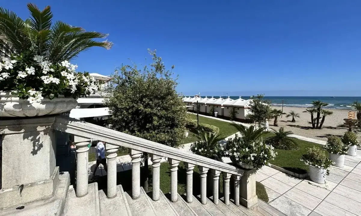 Scalinata in pietra con vasi fioriti, vista su una spiaggia ordinata con cabine bianche, tipica di una città di mare veneto.