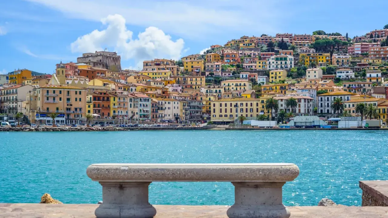 Panoramica di Porto Santo Stefano con case colorate a picco sul mare turchese. Un invito a scoprire cosa vedere a Porto Santo Stefano.