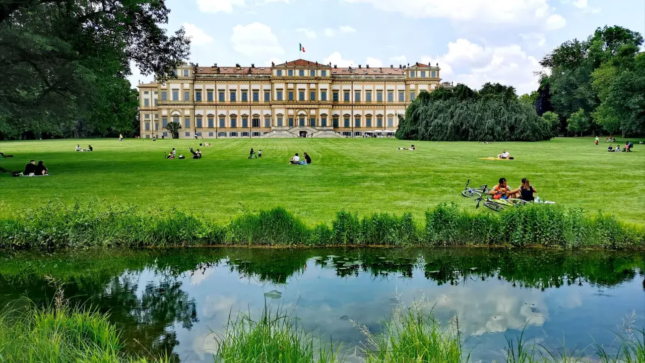 Villa Reale di Monza e il suo parco: un'idea per cosa vedere a Monza in un giorno. Persone rilassate sull'erba, un laghetto e il maestoso edificio.
