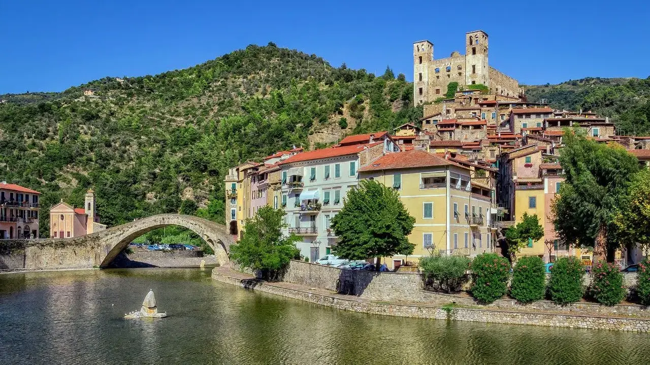 Borghi entroterra ligure levante: un ponte antico attraversa un fiume, case colorate si affacciano sull'acqua, un castello domina la collina verde.