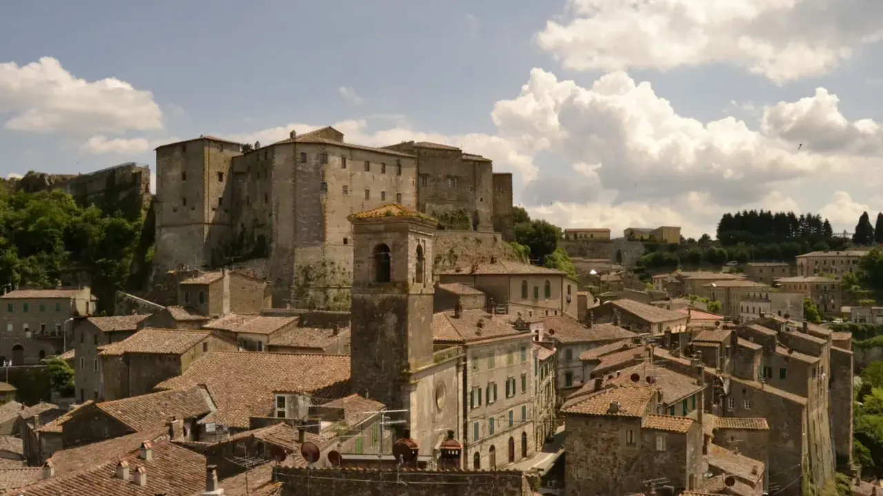 Panoramica di antichi borghi vicino Follonica, con un imponente castello in cima alla collina e un campanile che svetta tra i tetti rossi.