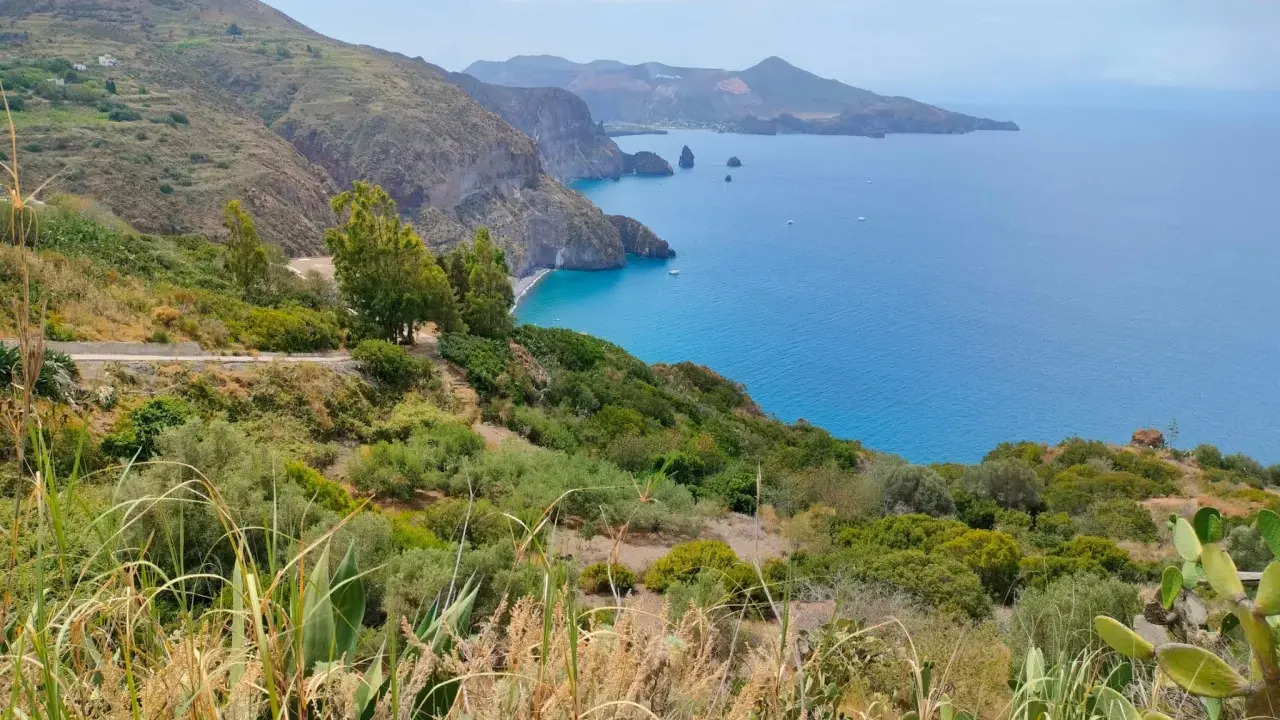 Panoramica mozzafiato per capire come visitare le Isole Eolie: costa verdeggiante, mare blu intenso e isole vulcaniche all'orizzonte.