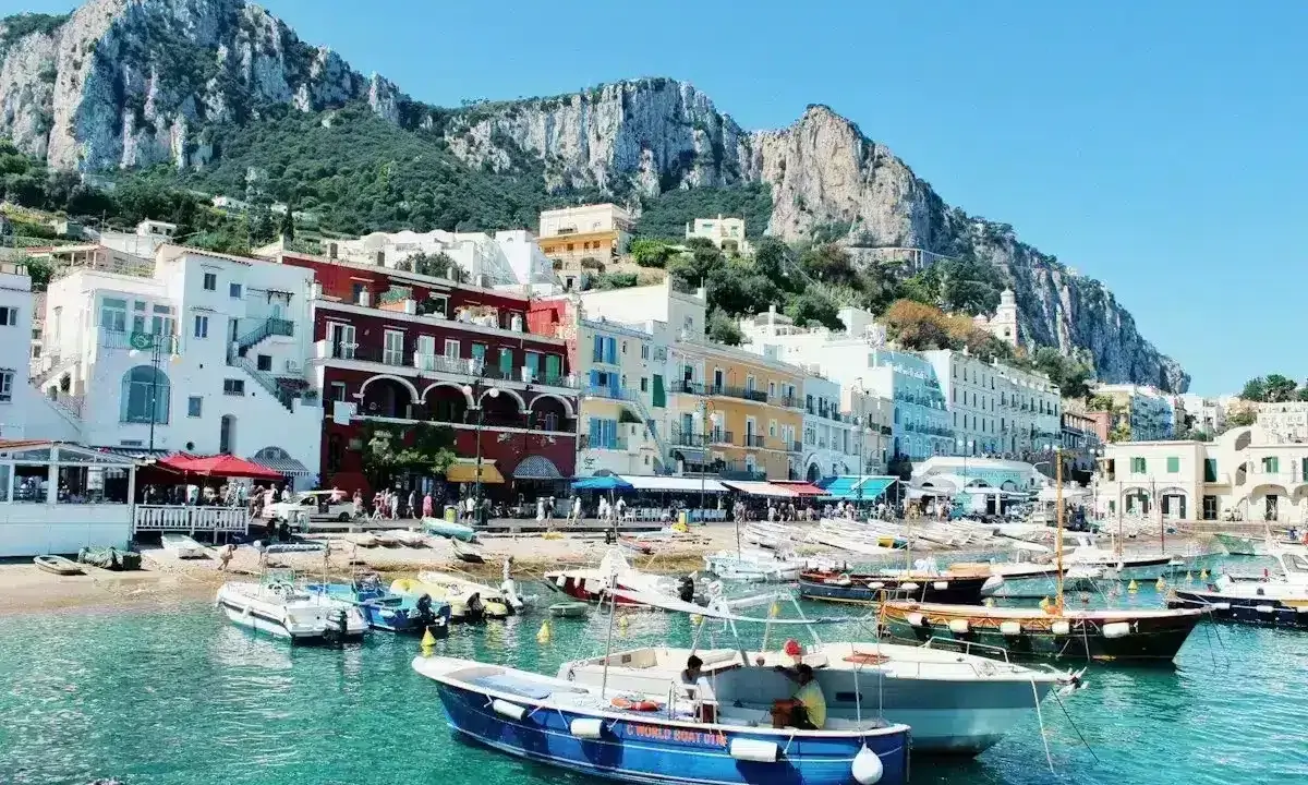 Colorate case affacciate sul mare turchese, con barche ormeggiate e montagne sullo sfondo. Un incantevole scorcio delle isole vicino Napoli.
