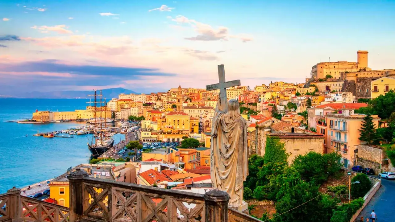 Una statua con una croce domina la vista di una città costiera colorata, perfetta per una gita fuori porta da Roma.
