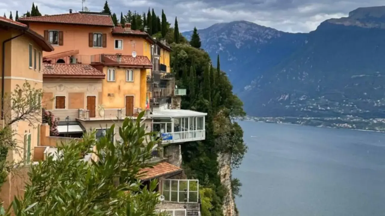 Case colorate aggrappate alla roccia a Tremosine sul Garda, con il lago e le montagne sullo sfondo.