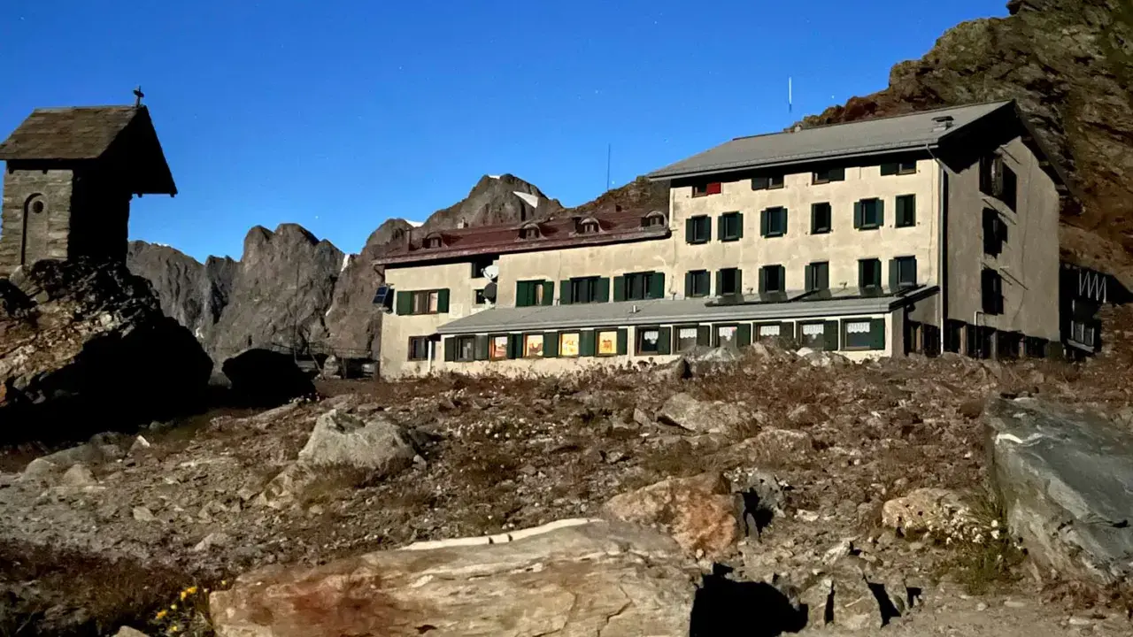 Rifugio alpino con piccola cappella, un esempio di cosa vedere in Lombardia, immerso in un paesaggio roccioso sotto un cielo stellato.