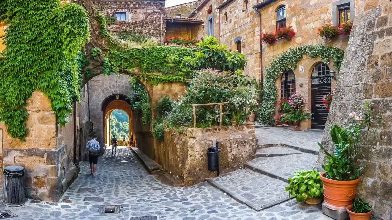 Un vicolo acciottolato tra antichi borghi da visitare nelle Marche, con case in pietra ricoperte di edera e fiori colorati.