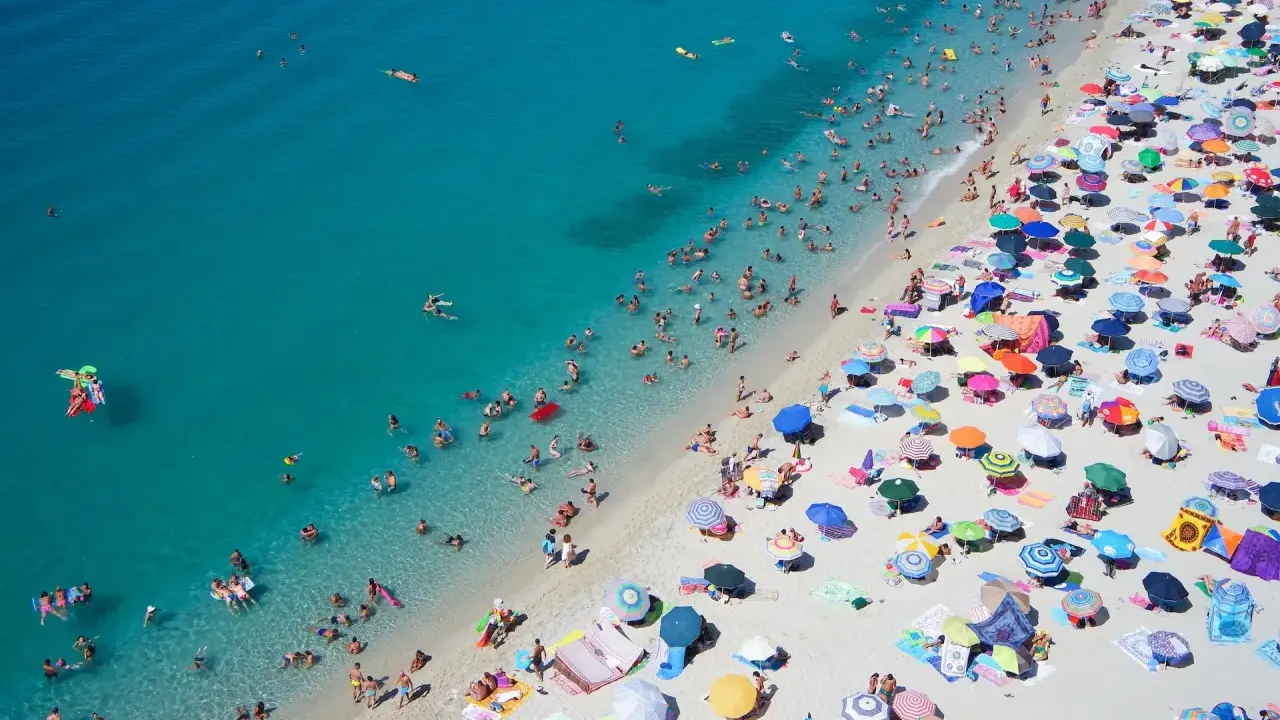 Spiaggia affollata con ombrelloni colorati e bagnanti nell'acqua cristallina, un'immagine perfetta per scoprire le località di mare più economiche in Italia.