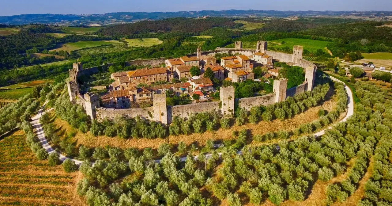 Borgo medievale fortificato su una collina, circondato da uliveti e vigneti. Bellissimi paesaggi toscani sotto un cielo azzurro.
