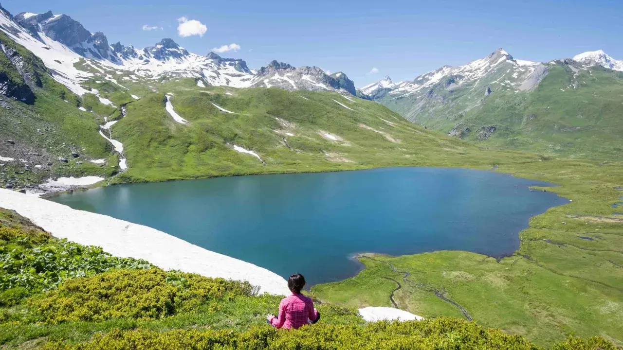 Pace e natura in Valle d'Aosta in estate: un lago alpino azzurro circondato da montagne innevate e verdi pascoli.