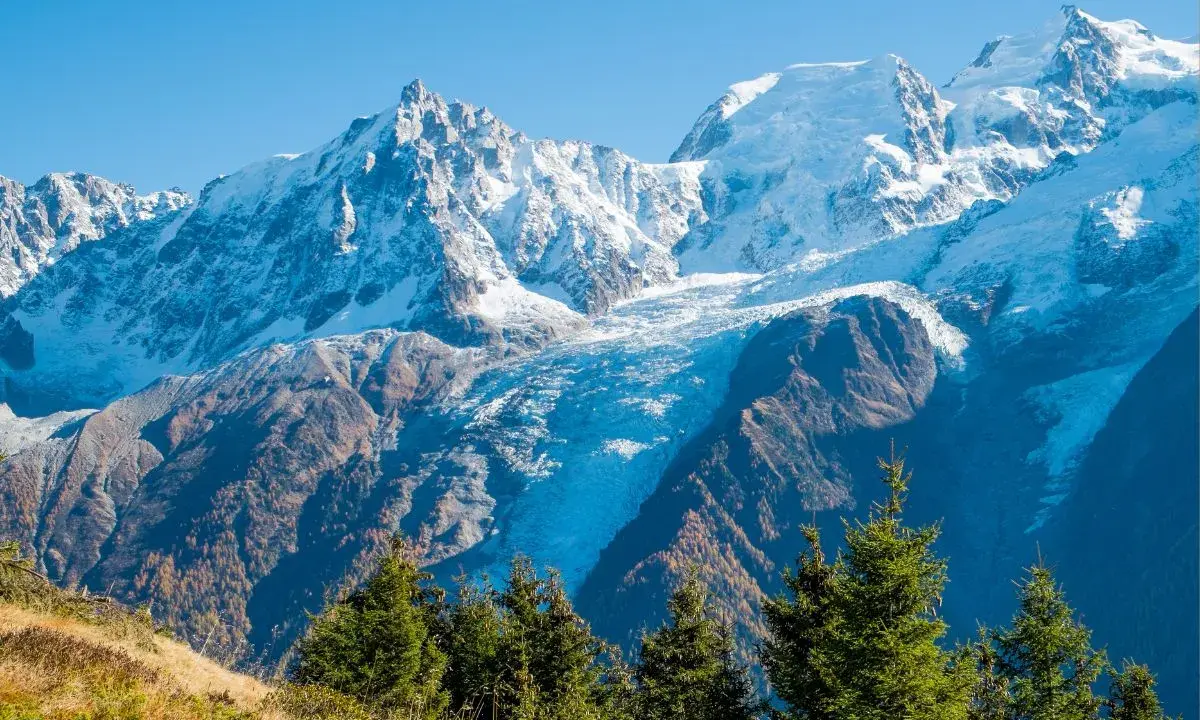 Ghiacciaio imponente tra le montagne italiane più famose, con cime innevate e boschi autunnali.