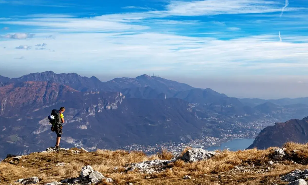 Escursionista ammira la vista panoramica di una montagna vicino Milano, con un lago e un paese in lontananza.