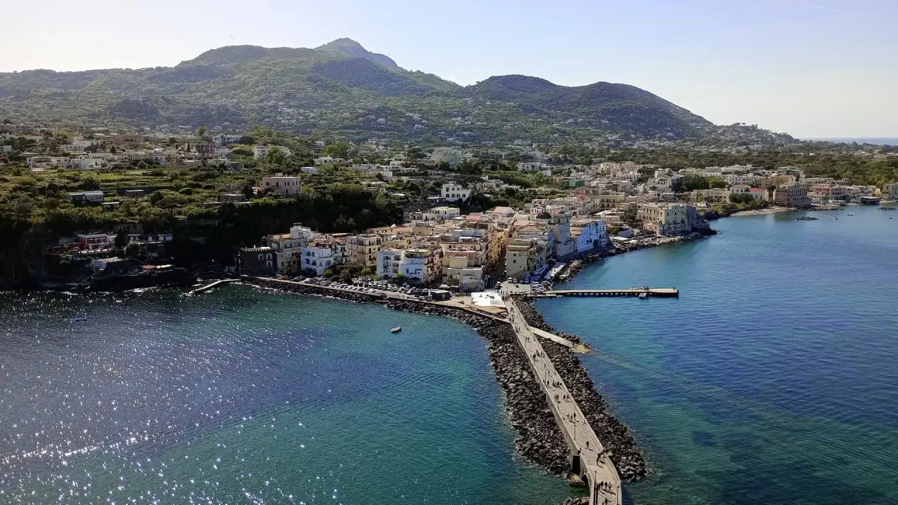 Ischia vista da Napoli: un borgo colorato si affaccia sul mare blu, con montagne verdi sullo sfondo.