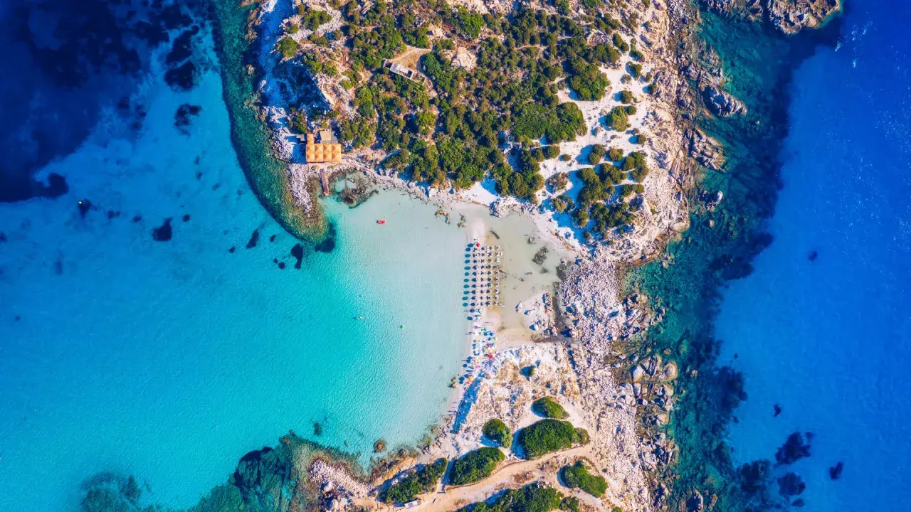 Spiaggia paradisiaca con acque cristalline, perfetta per itinerari Sardegna nord 7 giorni. Ombrelloni e lettini invitano al relax.