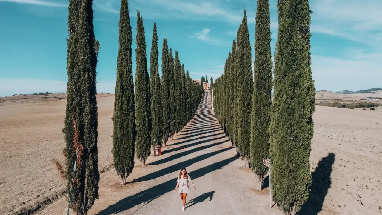 Viale di cipressi nel Val d'Orcia, un'icona da vedere in 3 giorni. Una donna cammina lungo la strada sterrata.