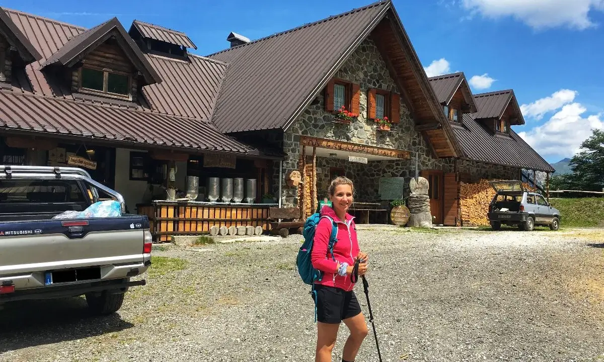 Ragazza con zaino e bastoncini da trekking davanti a un rifugio alpino, una delle tipiche malghe in Friuli.