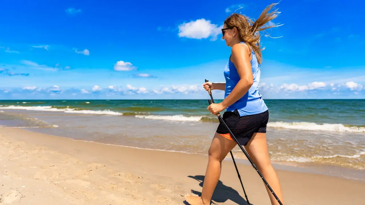 Donna con bastoncini da nordic walking in una splendida passeggiata al mare, con il vento che le scompiglia i capelli.