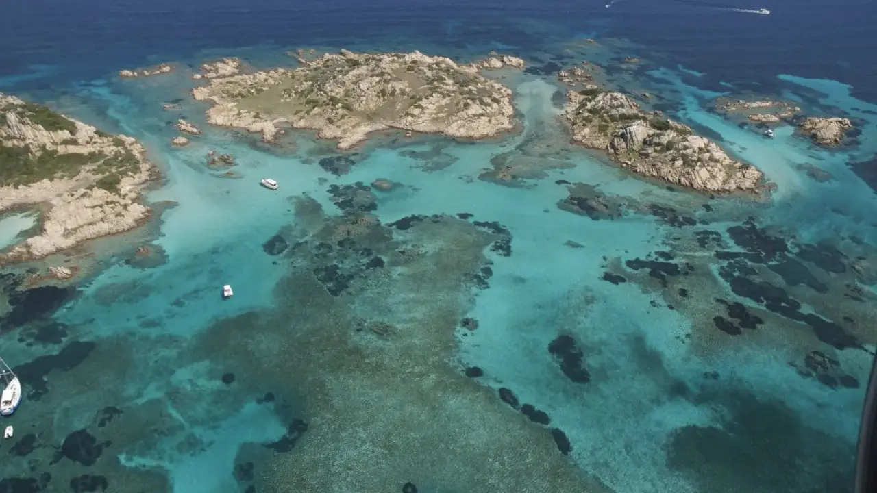 Acque cristalline e isolotti rocciosi, un paradiso dove si trova la Maddalena. Barche navigano in questo mare turchese.
