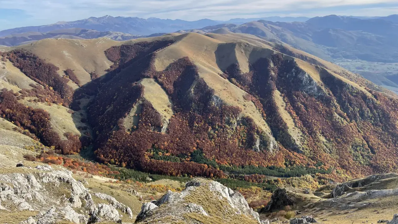Autunno nel Val di Norcia, con montagne dolci e boschi dai colori caldi che scendono verso la valle.