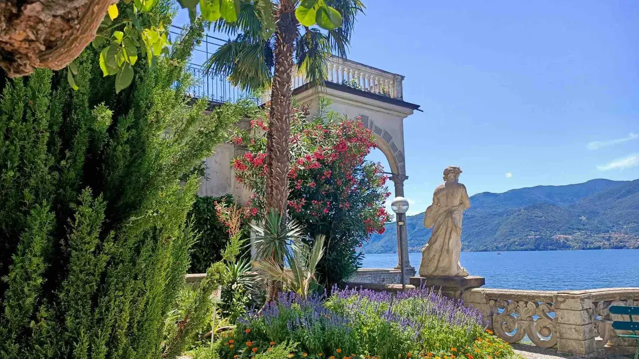 Giardino fiorito con statua e lago sullo sfondo, un angolo incantevole del varenna centro storico.