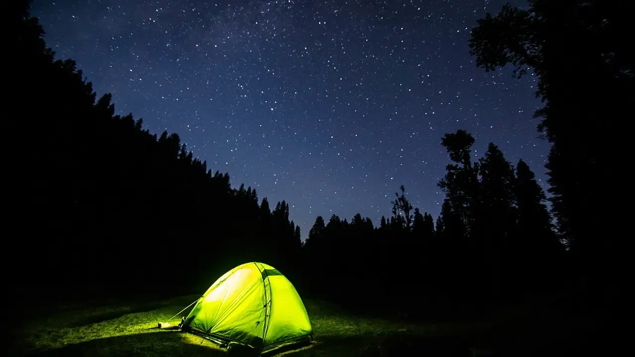 Tenda illuminata nella notte stellata, un invito a dormire in tenda immersi nella natura.