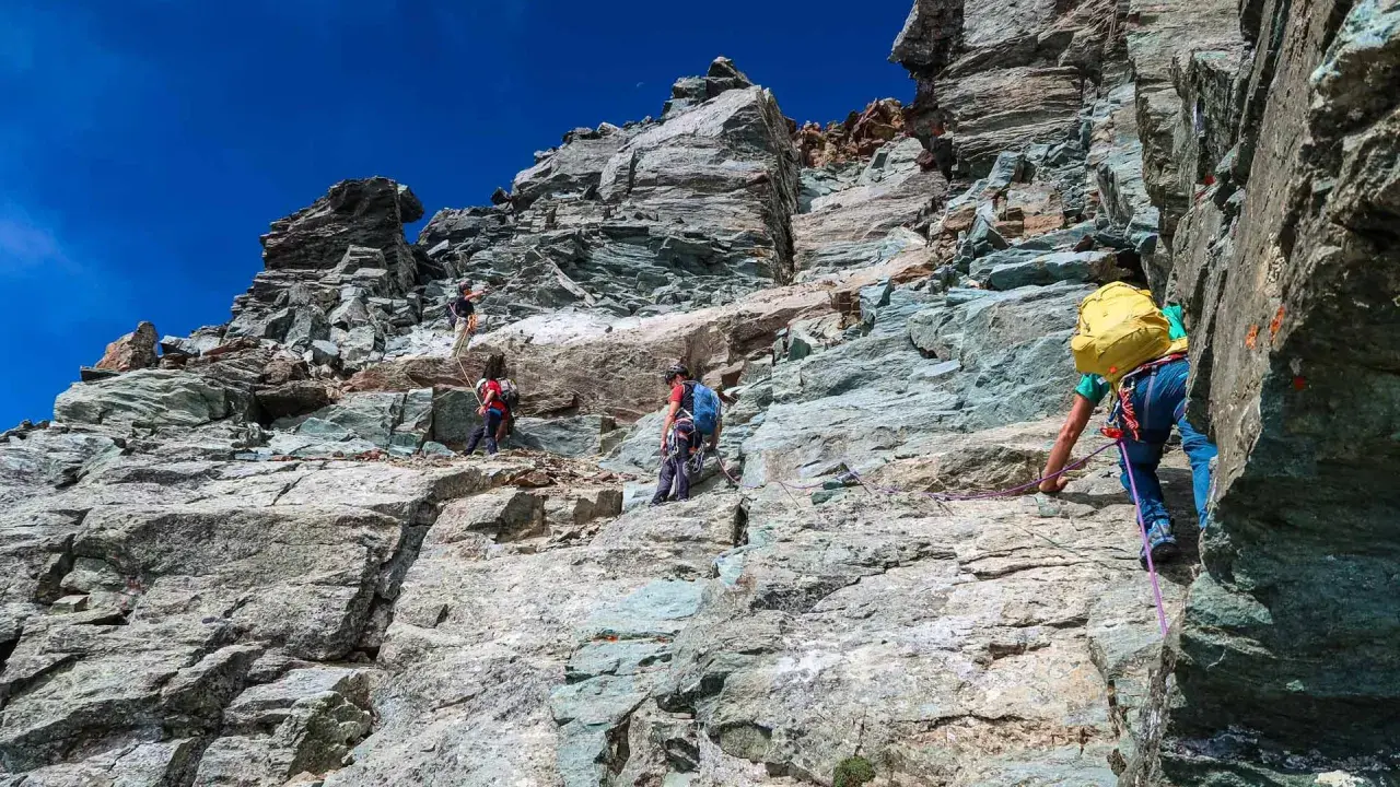 Alpinisti scalano la roccia sul Monviso, seguendo la via normale. Un'avventura sotto il cielo azzurro.