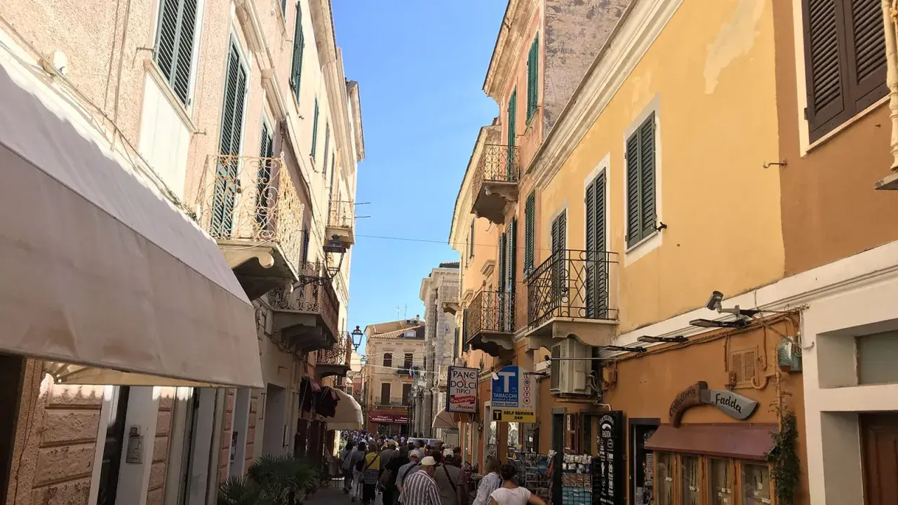 Passeggiata in un vicolo colorato, ideale per visitare La Maddalena in auto, con edifici storici e negozietti.
