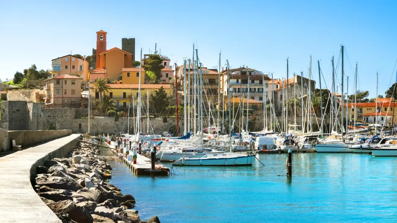 Porto turistico con barche a vela ormeggiate e case colorate che si affacciano sul mare, nel cuore del talamone centro storico.