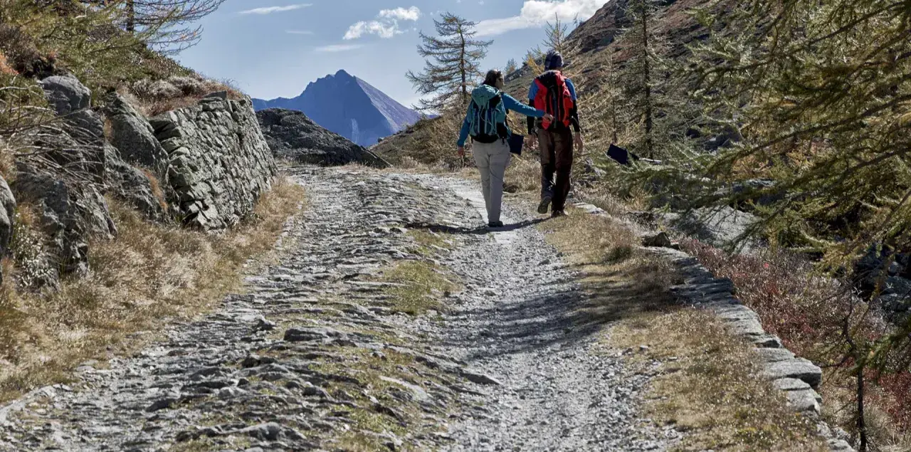 Escursionisti su sentiero sassoso nel Val di Susa, con montagne sullo sfondo.
