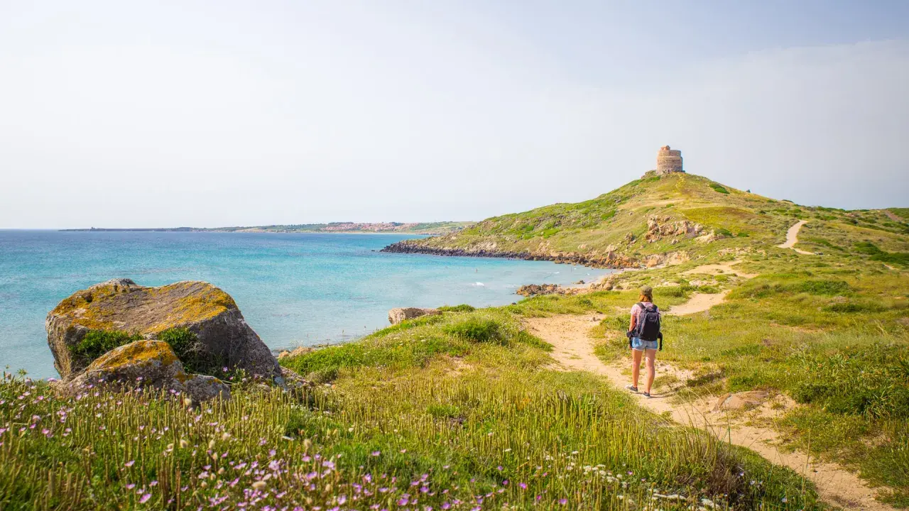 Sentiero panoramico per un tour Sardegna 7 giorni, con torre antica e mare turchese.