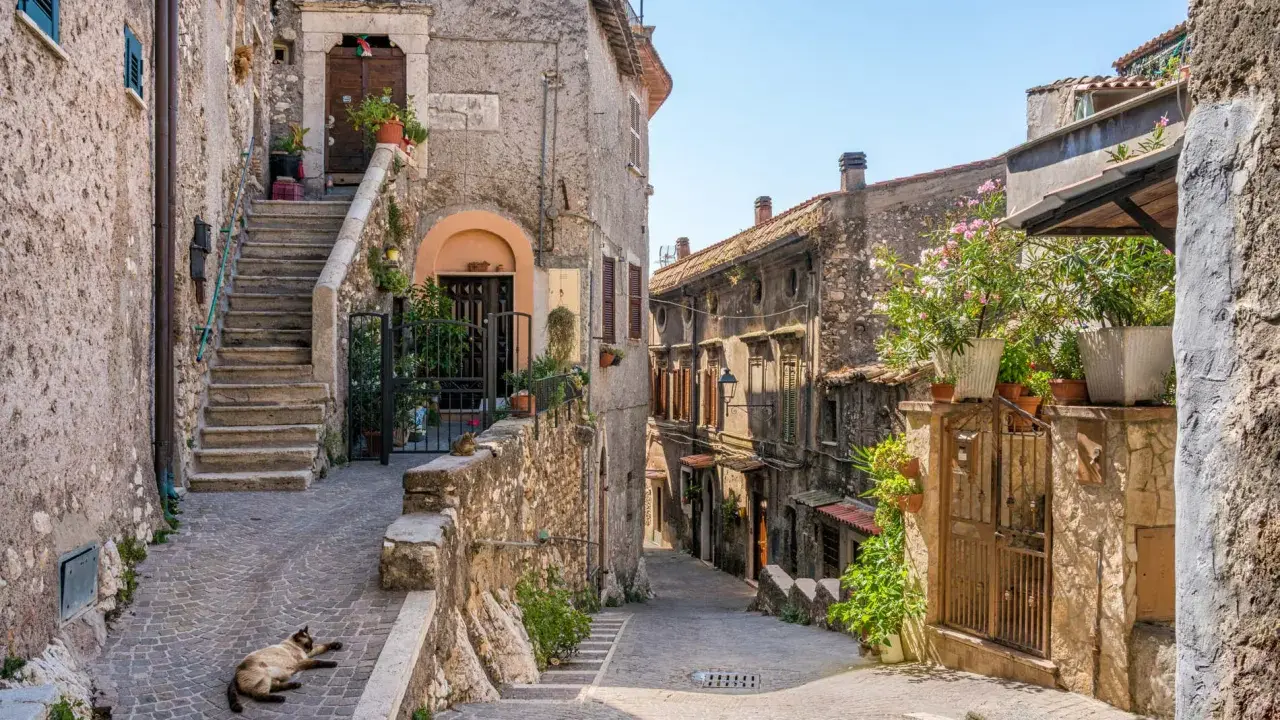 Un gatto si gode il sole in un vicolo acciottolato, tra antiche case di pietra e scale ripide. Un'atmosfera autentica di borghi da visitare nel nord Italia.