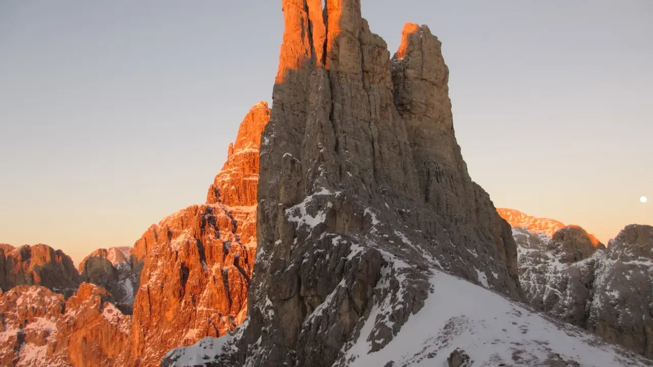 Le Torri del Vajolet illuminate dal caldo bagliore del tramonto, con la neve che ricopre le cime rocciose.