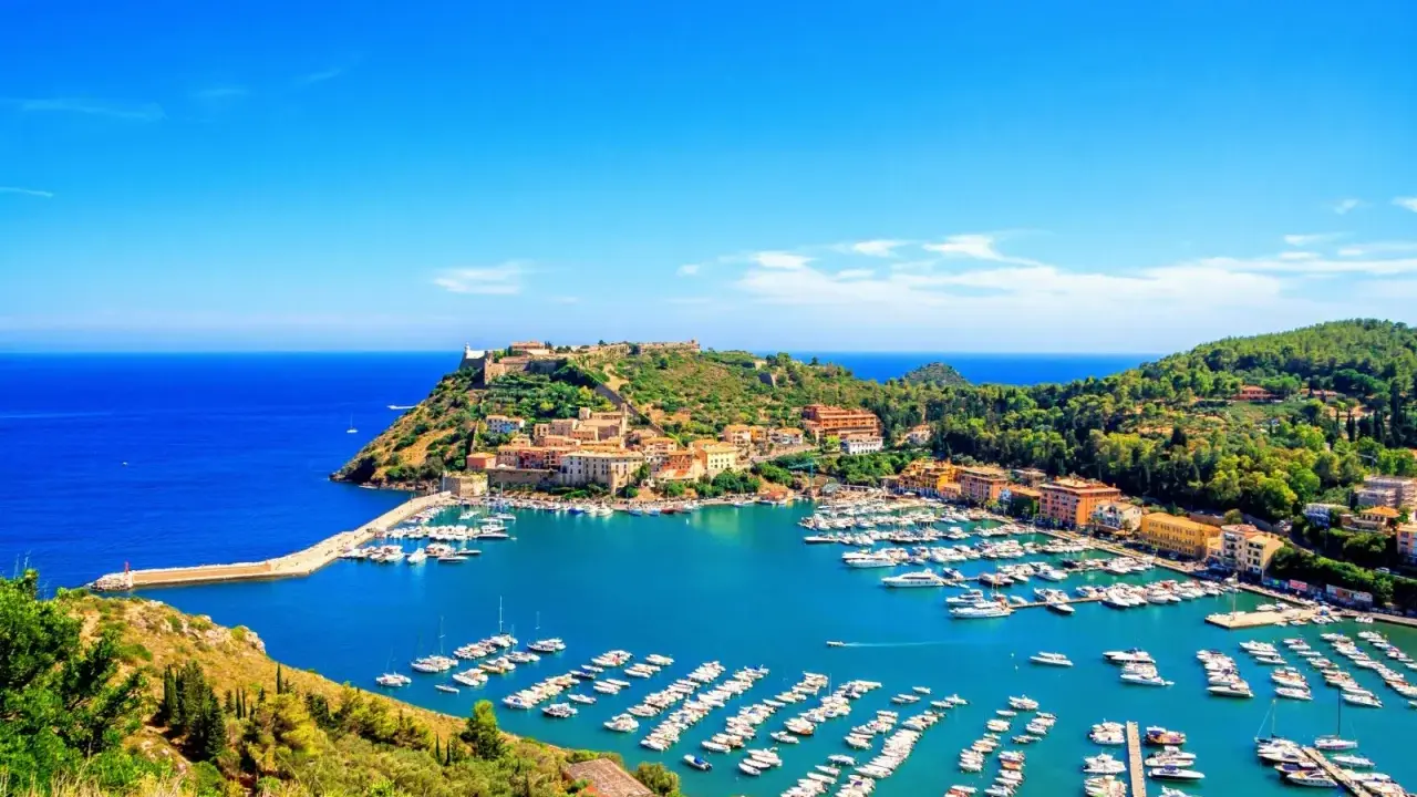 Porto Ercole, con le sue splendide spiagge e il porto pieno di barche, incanta sotto un cielo azzurro.