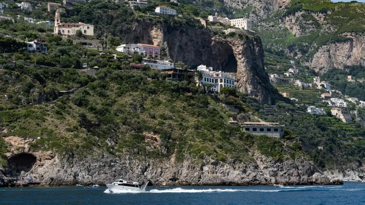 Un traghetto da Amalfi a Positano sfreccia nel mare blu, con case bianche aggrappate alle scogliere verdi.