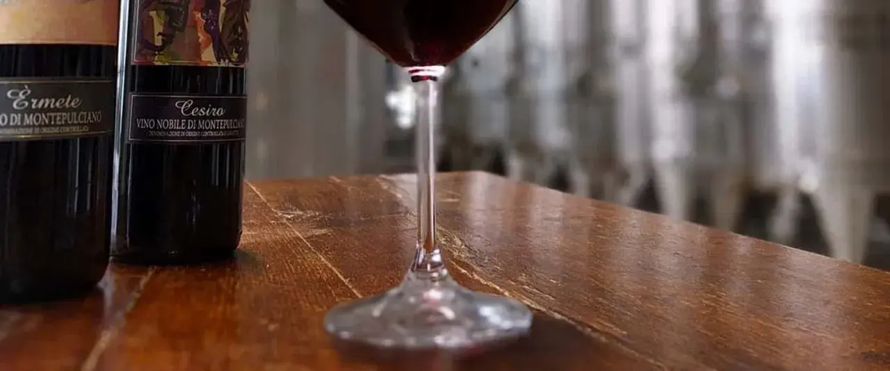 Bottiglie di Vino Nobile di Montepulciano e un calice di vino rosso, pronti per una degustazione vini toscana.