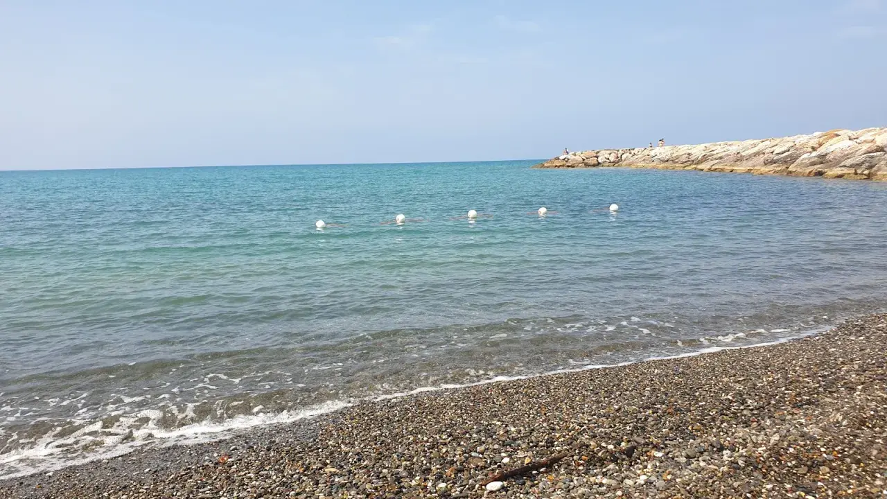 Spiagge più belle della Marina di Cecina: mare azzurro, ciottoli levigati e un molo roccioso con qualche bagnante.