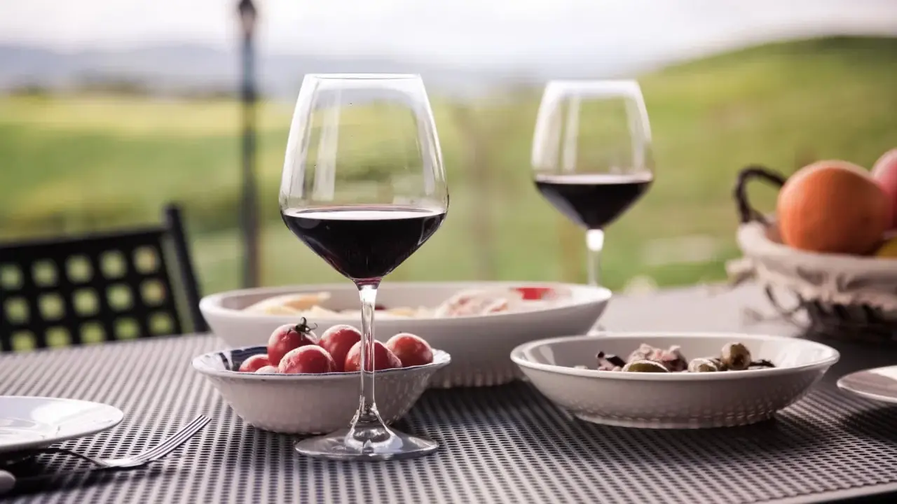Un bicchiere di vino rosso e stuzzichini su un tavolo all'aperto, con un paesaggio collinare sullo sfondo, perfetto per un percorso enogastronomico toscana.