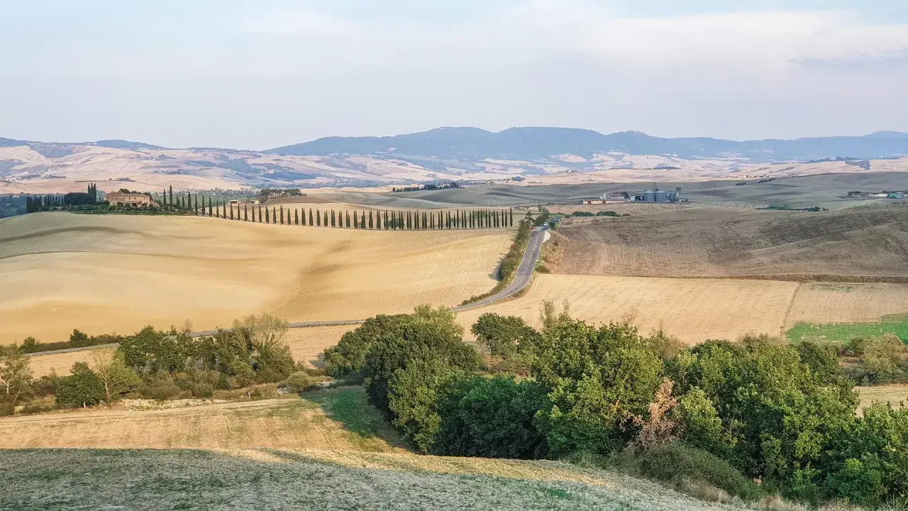 Colline dorate e cipressi iconici nel Val d'Orcia, con un borgo in lontananza. Un paesaggio da cartolina.