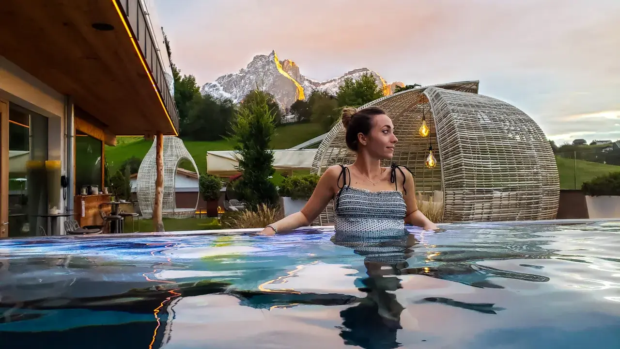 Donna rilassata in una piscina a sfioro con vista sulle montagne illuminate al tramonto, un'esperienza di benessere nelle terme in Trentino Alto Adige.