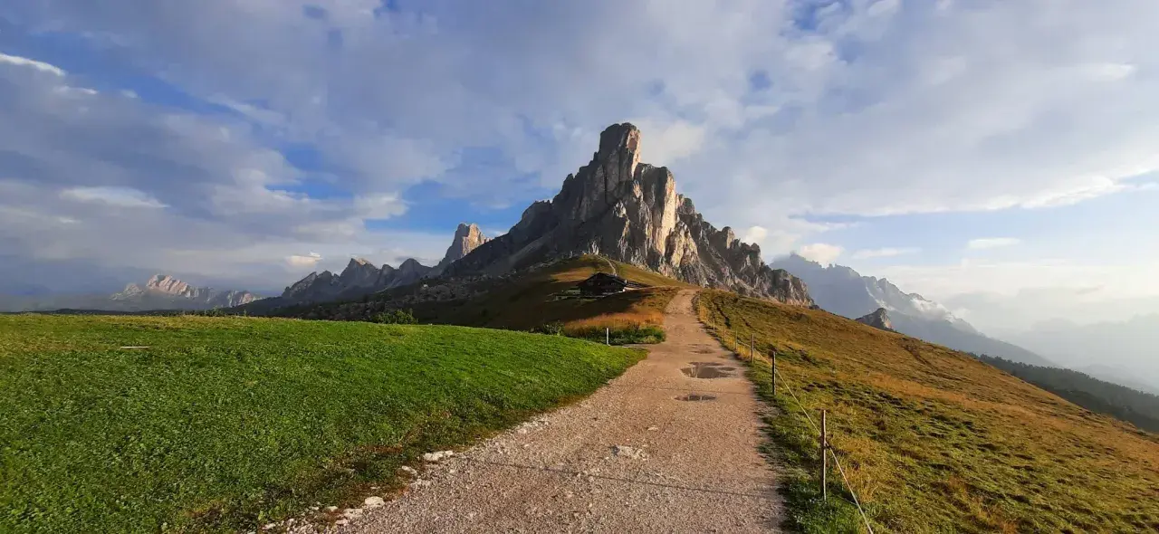 Sentiero per escursioni al Passo Giau, con imponenti vette rocciose e un rifugio alpino.