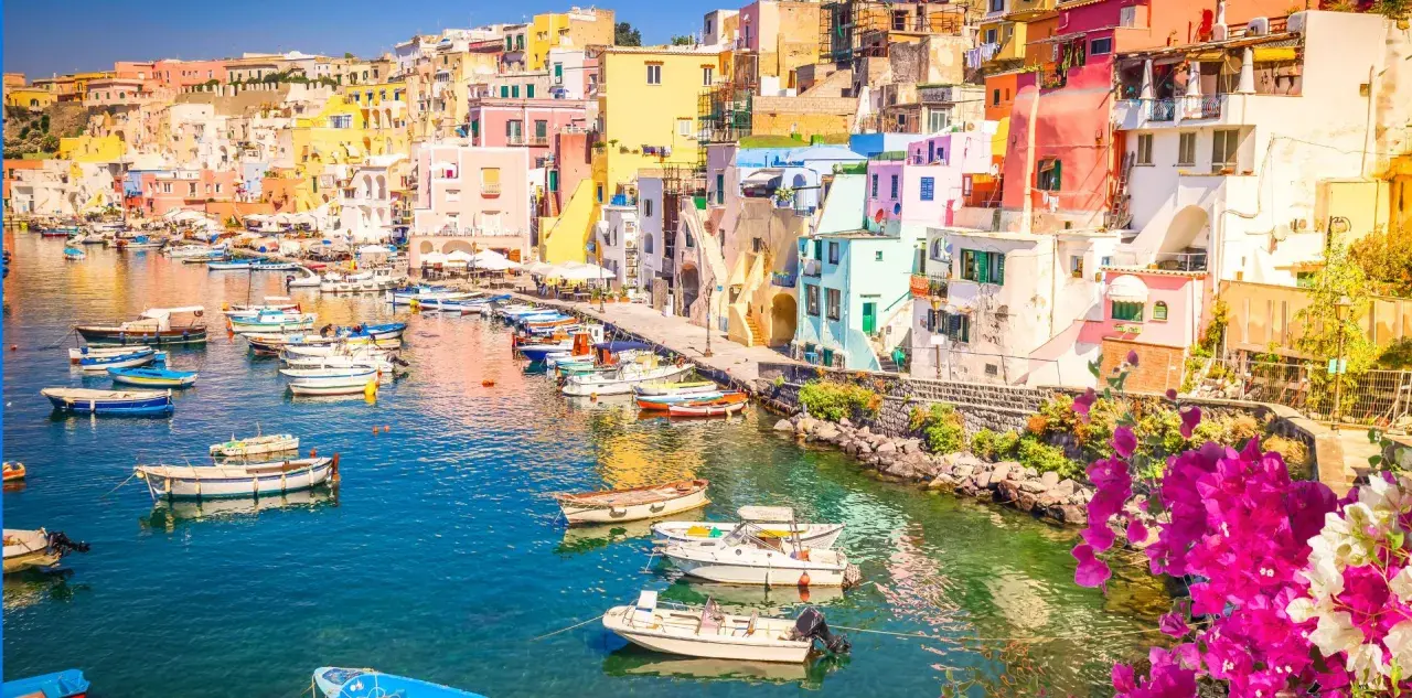 Porto di Corricella a Procida, un gioiello colorato. Ecco cosa vedere a Procida in un giorno: case pastello, barche nel blu intenso e bouganville in fiore.